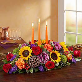 Low floral centerpiece with sunflowers, roses, and orange taper candles