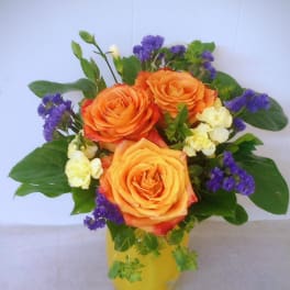 Orange roses with purple filler flowers in a yellow vase