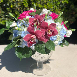Pink orchids and blue hydrangeas in a glass goblet vase