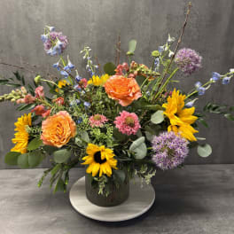 Mixed bouquet with orange roses, sunflowers, and purple allium in a glass vase