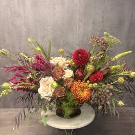 Large mixed floral arrangement in a dark vase with cream, red, and orange blooms