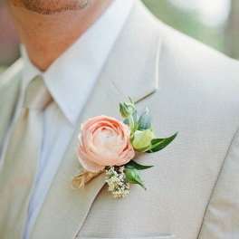Boutonniere with a blush ranunculus on a beige suit lapel