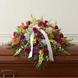 Colorful floral casket spray with red roses and a white ribbon
