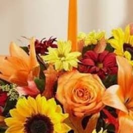 Colorful flower arrangement with sunflowers, roses, and lilies around a tall orange candle