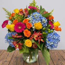 Colorful mixed bouquet in a clear glass vase with blue hydrangeas and roses