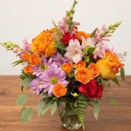 Mixed bouquet of orange roses, pink lilies, and purple daisies in a glass vase