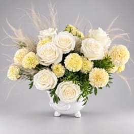 White roses and pale yellow carnations in a white vase with airy pampas grass