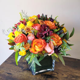 Colorful rose bouquet in a square glass vase on a wooden table