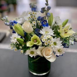 Bouquet of white daisies, cream roses, and blue flowers in a glass vase