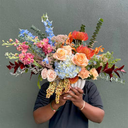 Large mixed bouquet in a white vase with peach roses and blue hydrangea
