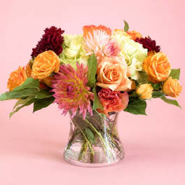 Mixed bouquet of orange, pink, and burgundy flowers in a clear glass vase