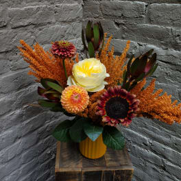 Mixed floral arrangement in a yellow vase with orange accents