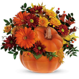 Autumn floral arrangement in a pumpkin-shaped container with orange and burgundy blooms
