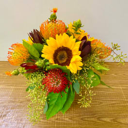 Sunflower bouquet with orange and red pincushion blooms on a wooden surface