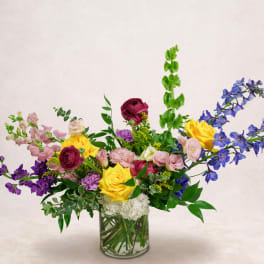 Mixed bouquet of roses, snapdragons, and blue delphinium in a glass vase