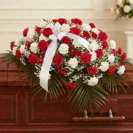 Red and white carnation casket spray with a white ribbon