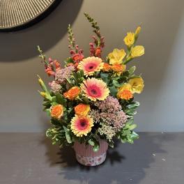 Mixed bouquet in a pink decorative pot with orange and yellow blooms