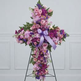 Cross-shaped floral tribute with pink and purple flowers and a lavender ribbon