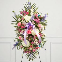 Tall floral standing spray with pink, white, and purple blooms and a lavender ribbon