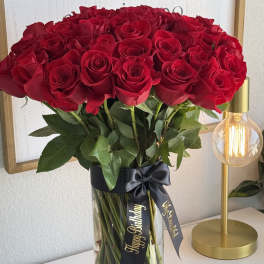 A tall vase of red roses tied with a black ribbon