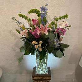 Tall mixed bouquet with pink lilies, roses, and blue flowers in a glass vase