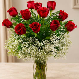Red roses arranged in a clear glass vase with white baby's breath