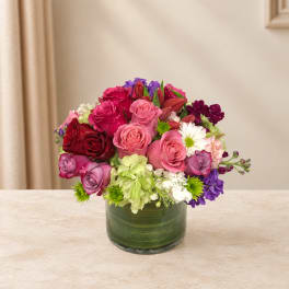 Mixed bouquet of pink, red, white, and purple flowers in a green glass vase