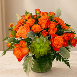 Orange roses and gerbera daisies in a glass vase with a green succulent accent