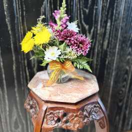Small mixed flower bouquet in a clear glass vase with an orange ribbon