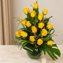 Yellow roses arranged in a glass vase with greenery