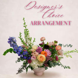 Colorful mixed flower arrangement in a pale vase with tall blue blooms