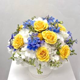 Yellow roses and blue flowers arranged in a white vase