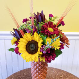Mixed bouquet with sunflowers and burgundy blooms in a textured vase
