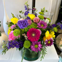 Colorful mixed bouquet in a green glass vase with purple, pink, and yellow blooms