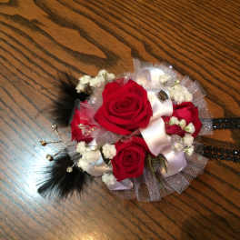 Red rose corsage with white ribbon and black feather accents