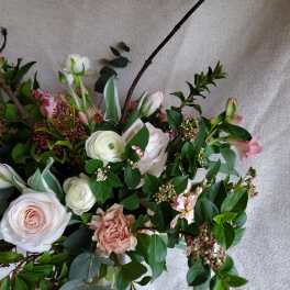 Loose arrangement of blush roses, white ranunculus, and pink flowers with branching accents