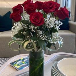 Red roses arranged in a tall glass vase with white baby's breath