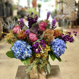 Colorful bouquet with blue hydrangeas, pink roses, and purple flowers in a glass vase