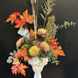 Autumn floral arrangement in a white vase with orange leaves and chrysanthemums