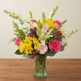 Mixed bouquet of pink, yellow, white, and purple flowers in a glass vase