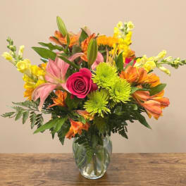 Mixed bouquet in a glass vase with pink roses, lilies, and bright yellow flowers