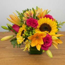 Bright mixed bouquet with sunflowers, pink roses, and orange lilies in a glass vase