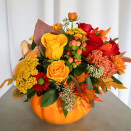 Orange pumpkin vase filled with red and yellow roses and autumn flowers