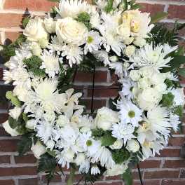 White floral wreath on a black stand with roses and daisies