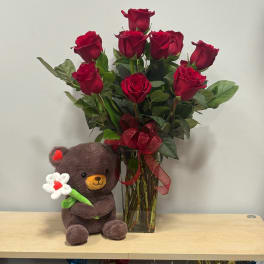 Red roses in a glass vase with a teddy bear holding a flower