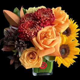 Orange roses, red chrysanthemums, and sunflowers in a glass vase