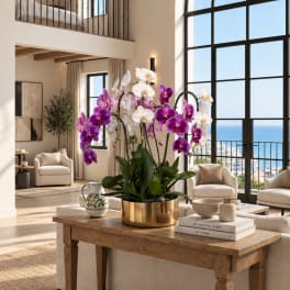 Purple and white orchids arranged in a gold planter on a coffee table