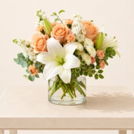 Peach roses and white lilies arranged in a clear glass vase