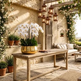 White orchids in a gold bowl on a wooden table in a patio setting