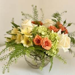 Mixed bouquet of roses, hydrangeas, and pale yellow flowers in a glass bowl vase